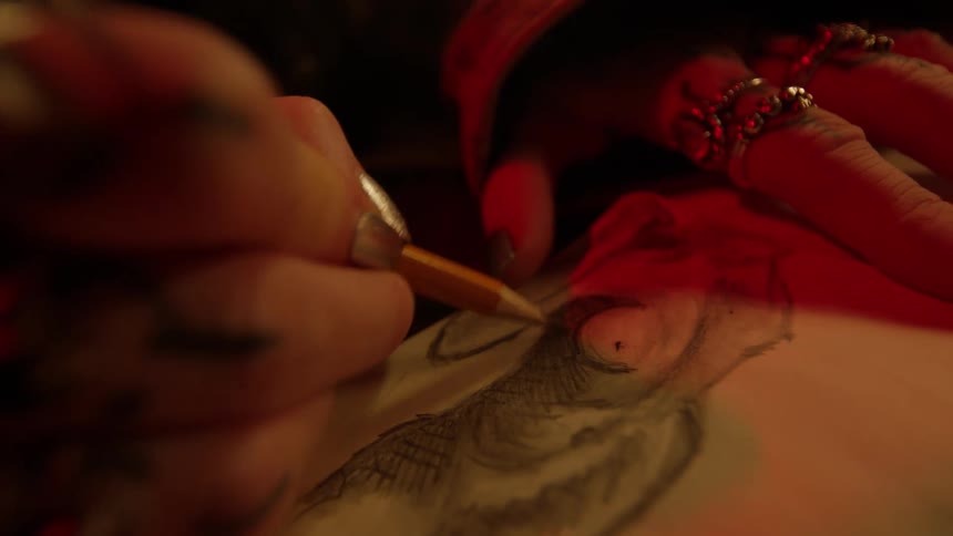 A womans hands are shown full of rings as she sketches a rabbit in pencil