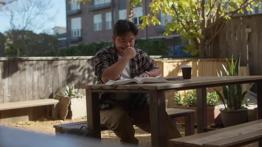Man sitting in the backyard at a wooden table stretching and writing