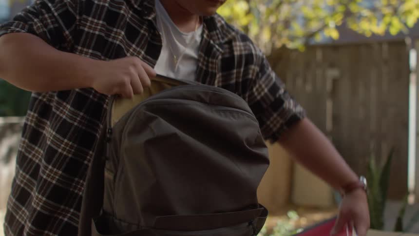 Man sets a backpack on a picnic table and pulls out a book and notebook to study