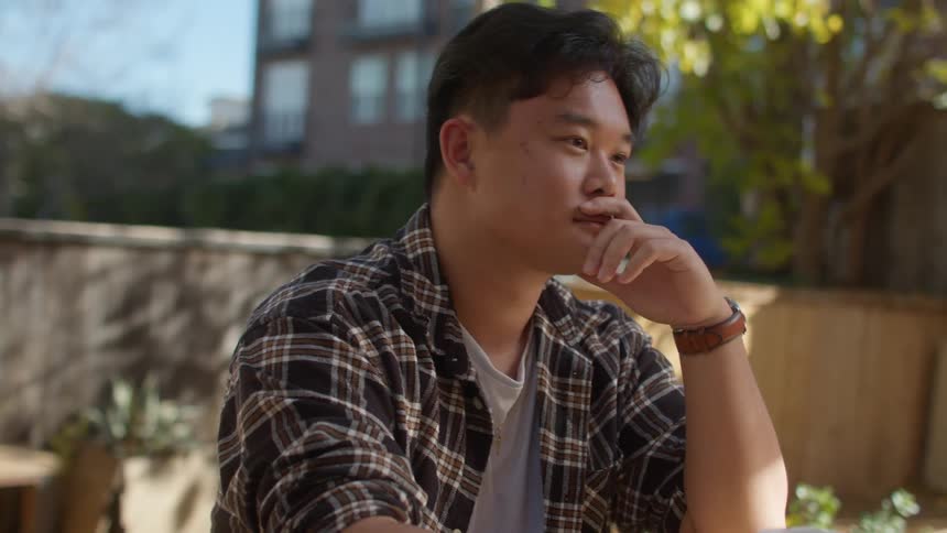 Man holds disposable coffee cup on table while listening intently to the person sitting across from him