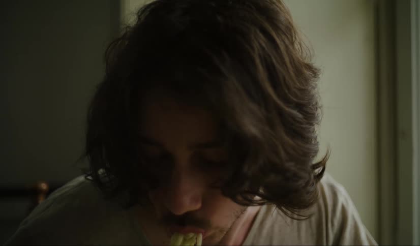 A young man with long hair chews while eating a meal with noodles