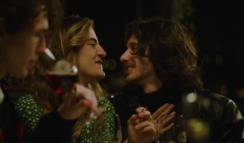 A man and woman sharing an intimate moment while another man leisurely sips a glass of wine