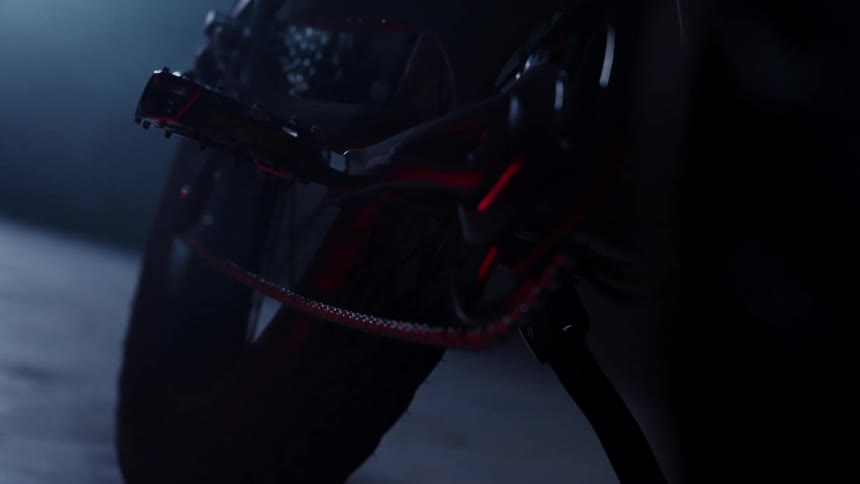 A motorcycle is stopped in a dark environment and its tire is highlighted