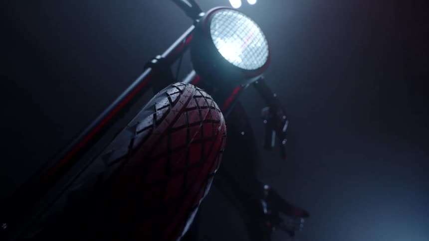 Motorcycle with its headlight on sits parked in darkness brightenend by lightsource