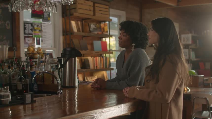 Two women place an order at a bar while resting their hands on the chunky wood counter