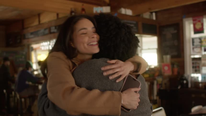 Woman stands to greet friend arriving at pub