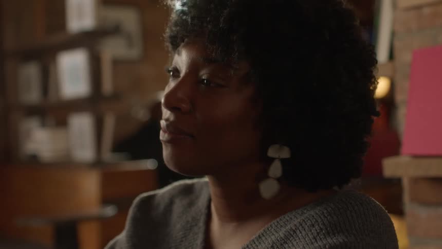 A woman takes a sip of her coffee and then smiles and nods while listening