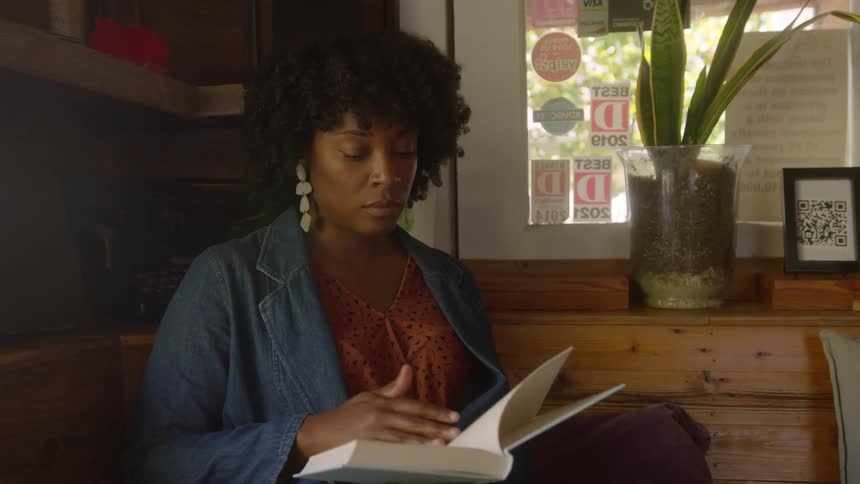 Woman with curly hair earrings and a blue jacket reads a book