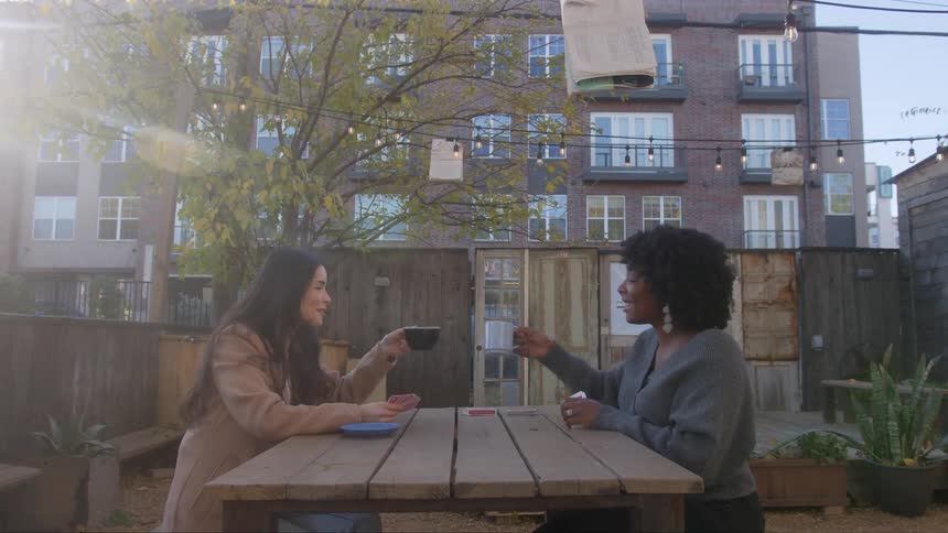 Women seated at a table in the cafe yard share smiles and engage in conversation with each other