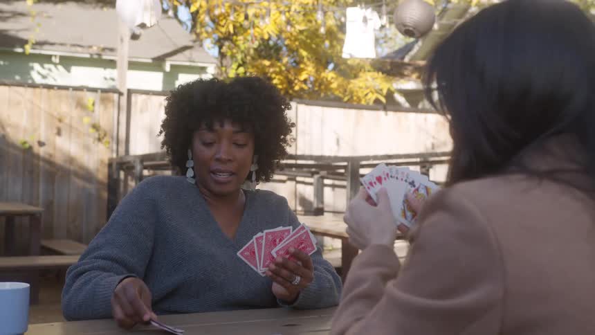 Seated at a table in the cafe yard women share smiles engage in conversation and enjoy a card game together