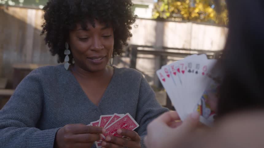 Seated at a table in the cafe yard women share smiles engage in conversation and enjoy a card game together