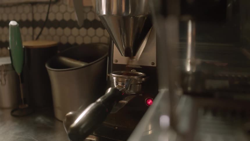 Coffee grounds pour from a professional grinder into an espresso measuring spoon