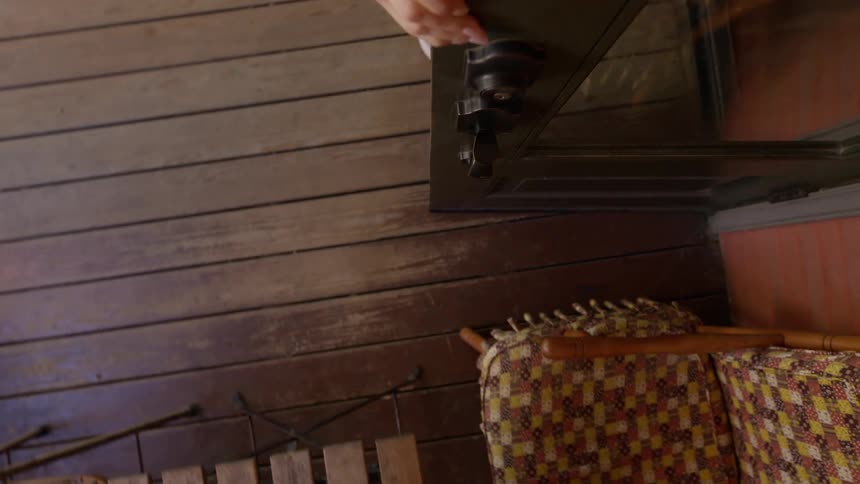 A woman on a deck opens a door to a house and walks inside