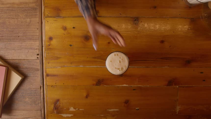 Server puts down full beer on wooden surface and man picks it up
