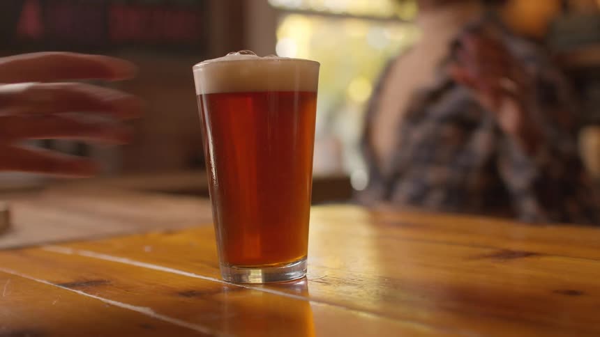 A bartender serves a man a beer in a tall glass at a bar