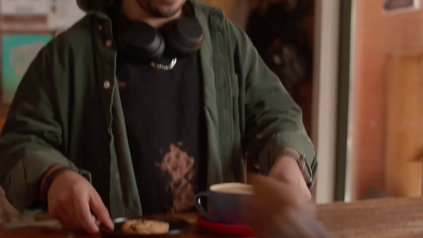 Man picks up cookie and coffee from server at counter before heading toward the door
