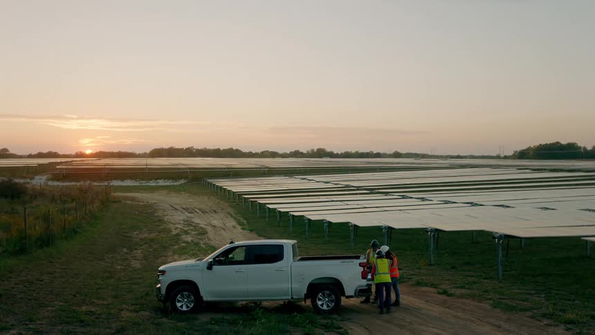 Utility workers are standing at the rear of a white pickup truck at a solar farm