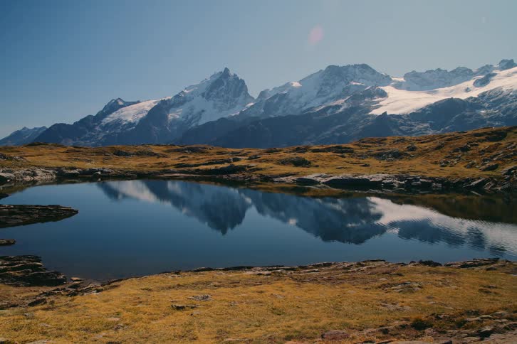 A landscape of a still lake and snowy mountains behind