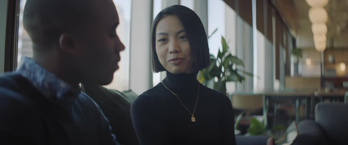 A young woman holds her smart phone conversing with her male colleague