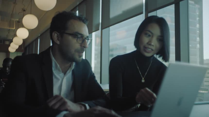 Two office workers look at a laptop together
