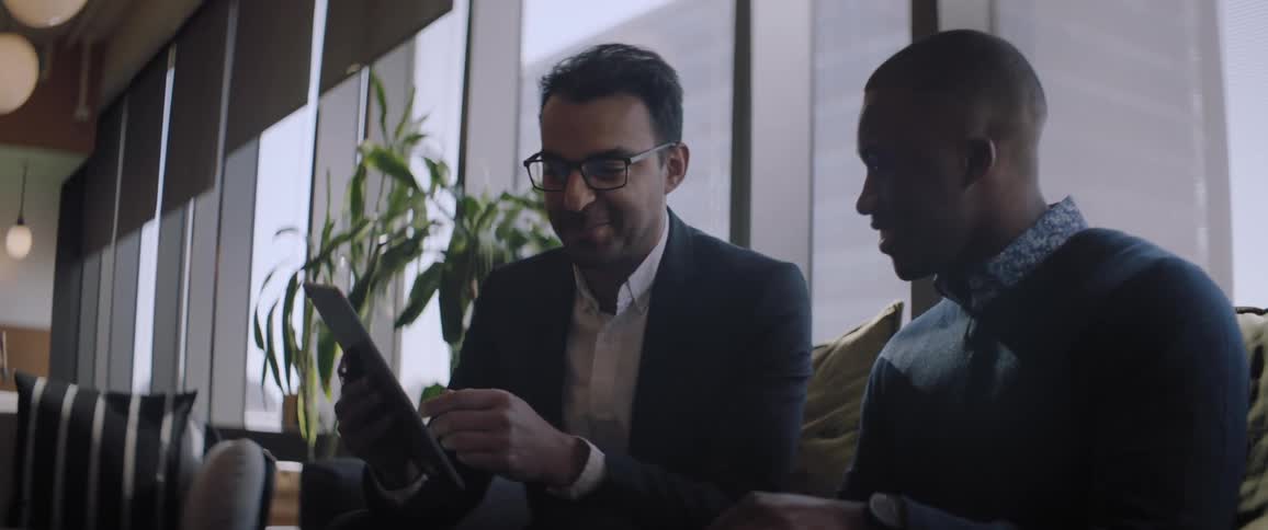 Two men talking while looking at a tablet in a large dining room