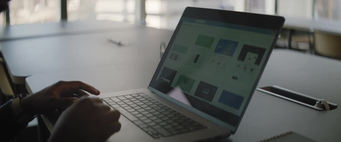 A notebook with a screen on is on a table and a persons hands are on the keyboard