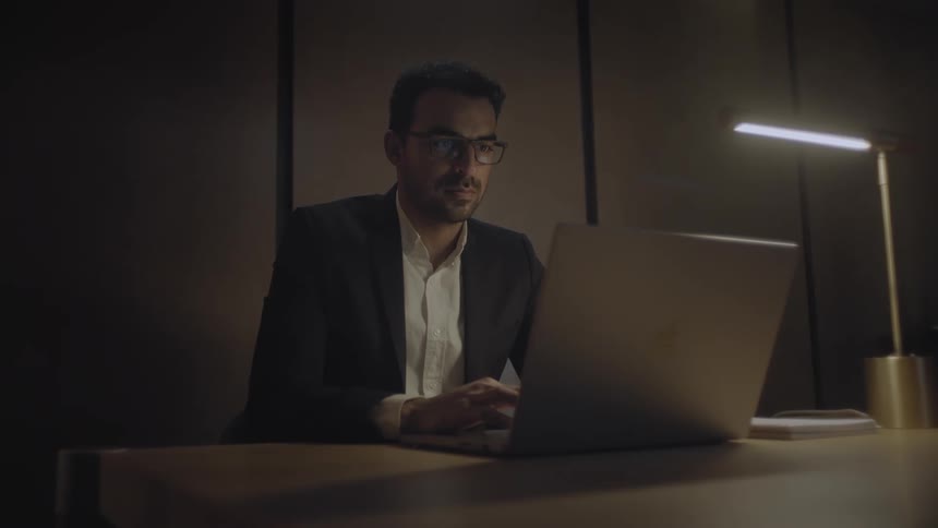 Male adult sits at a table typing on a laptop in a minimalist style office with a single desk lap