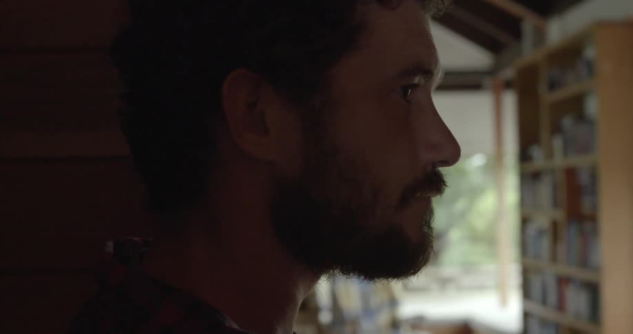 a bearded person gazing up while standing in a domestic setting.