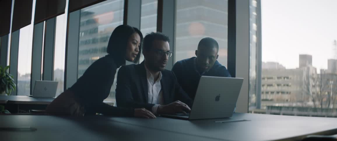 Women and two men work on laptop in office near window