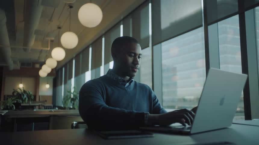 A man is smiling while sitting and using a laptop