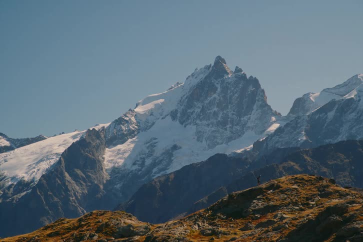 A person hiking to the top of the mountain with a snow filled mountain in the background