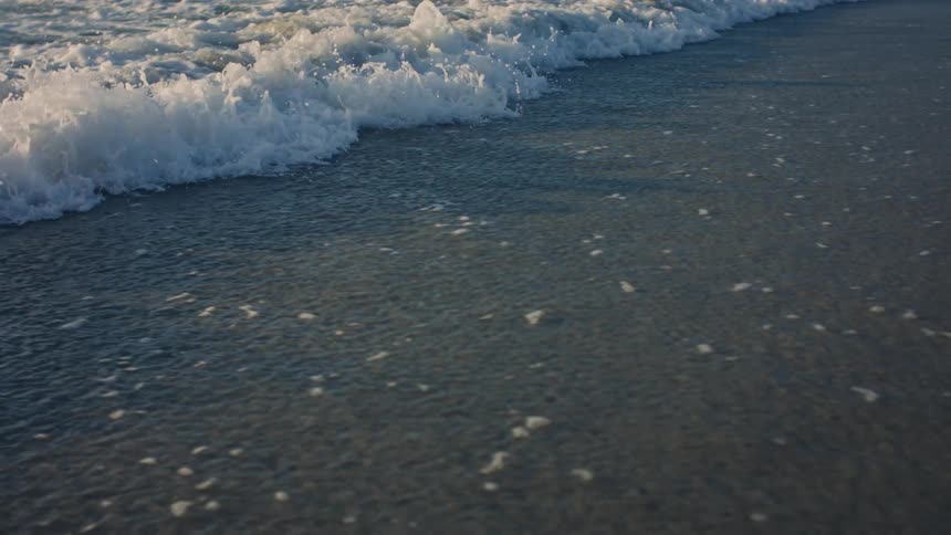 Small waves breaking and reaching the shore of the beach