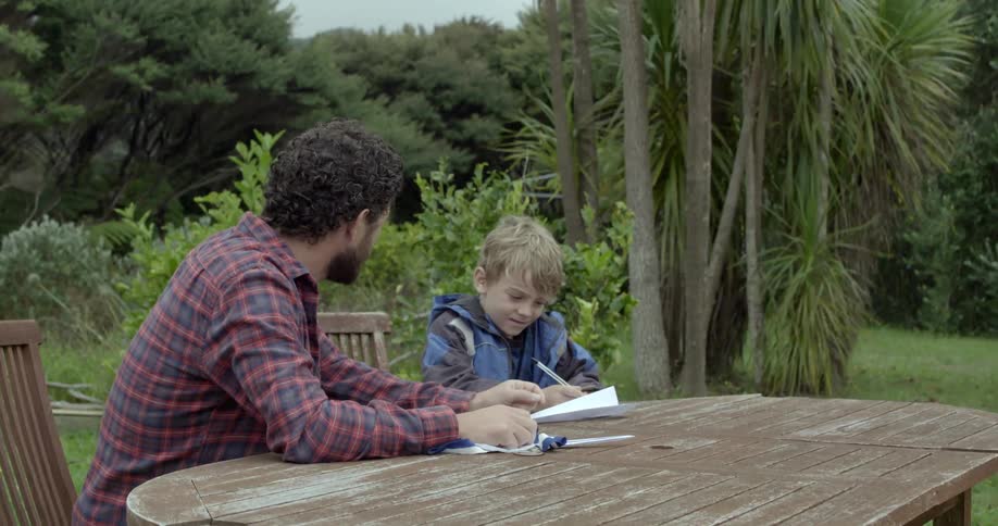 A man and small boy sitting together outside while working on a craft project.