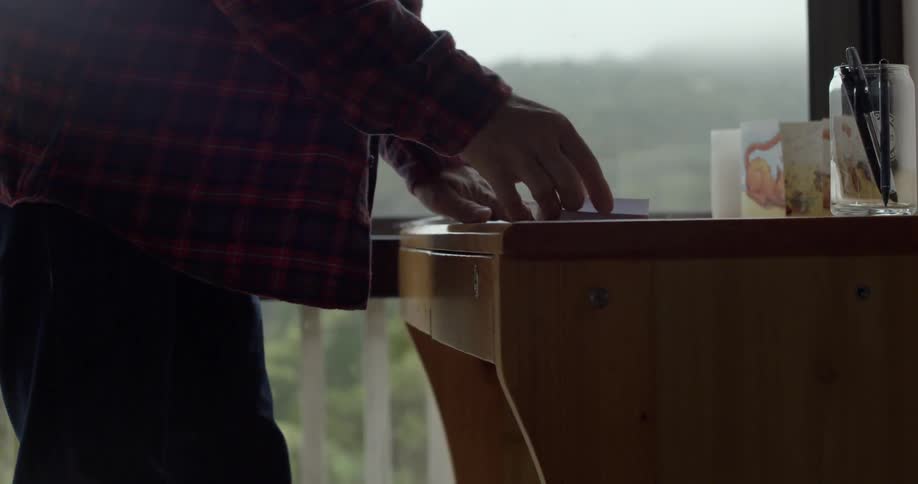A man opens a desk drawer and removes a paper and folds it
