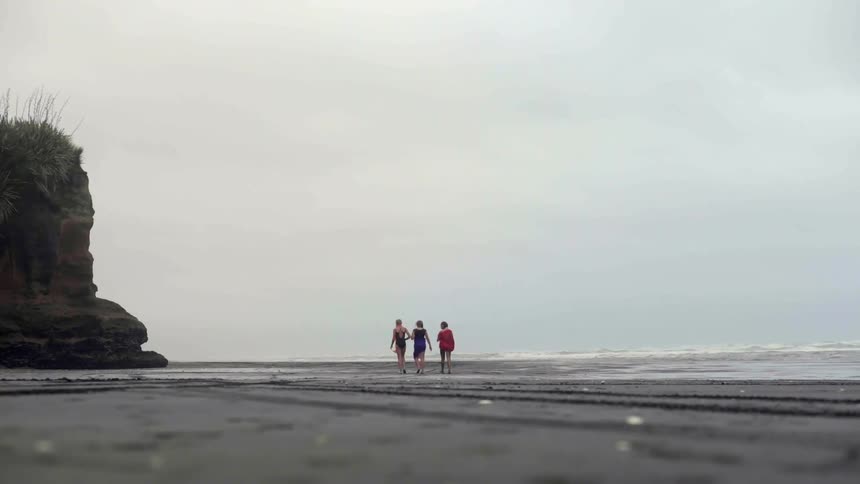 A group of close friends walks along a dramatic beach during a coastal getaway.