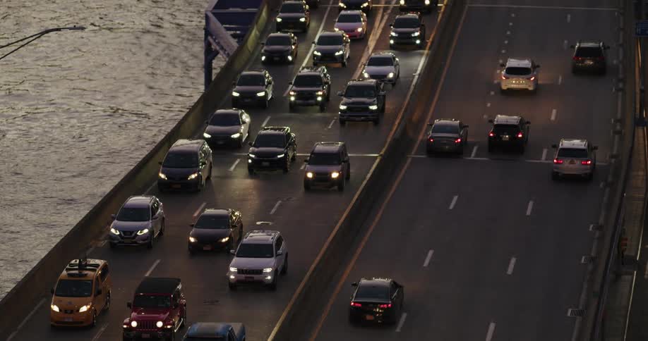 Vehicles with headlights drive on a bridge over a river
