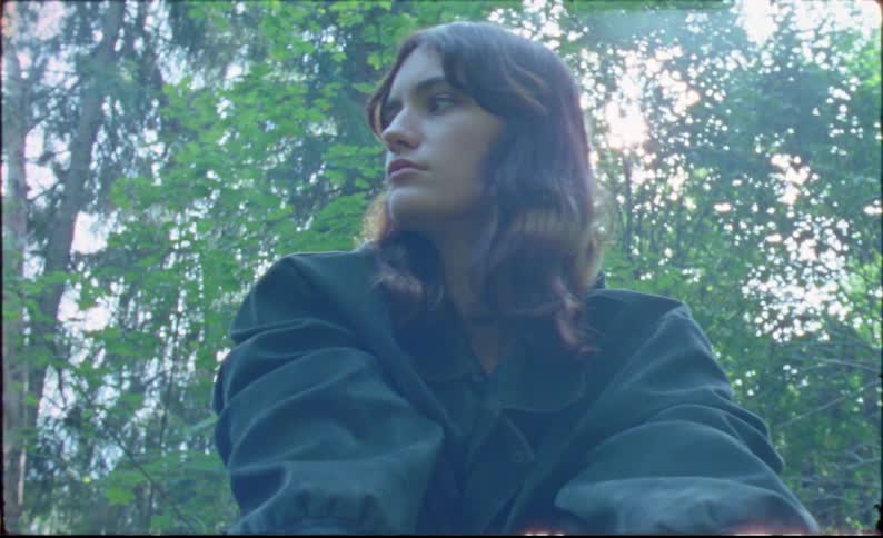 A young woman crouches atop a mossy log in the forest