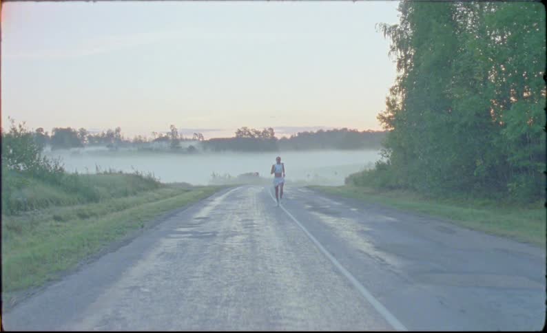 A woman is running fast by trees on a foggy rural road