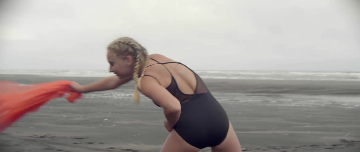 A young woman dances on the beach twirling a red piece of fabric