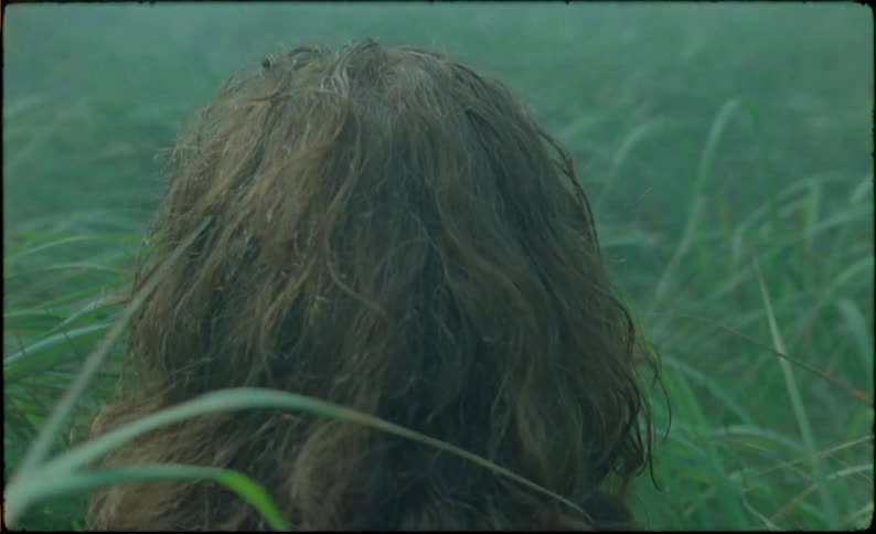 A boy crouched in a meadow during a cloudy day