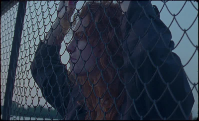 Young woman reclined on a wire fence near the lake