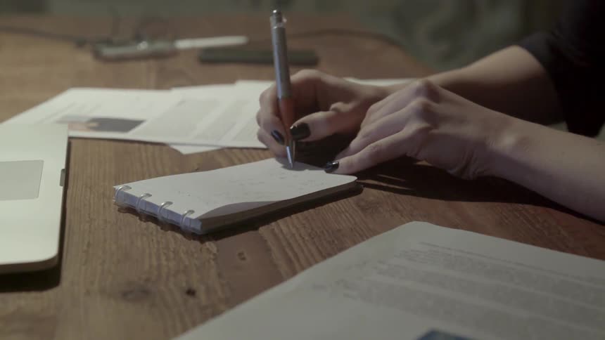 A woman with a silver pen writes in a small notebook during office hours.
