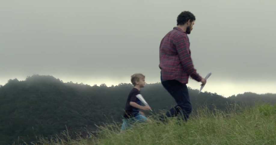 A man and his young son hike up a misty grassy hill together outdoors.