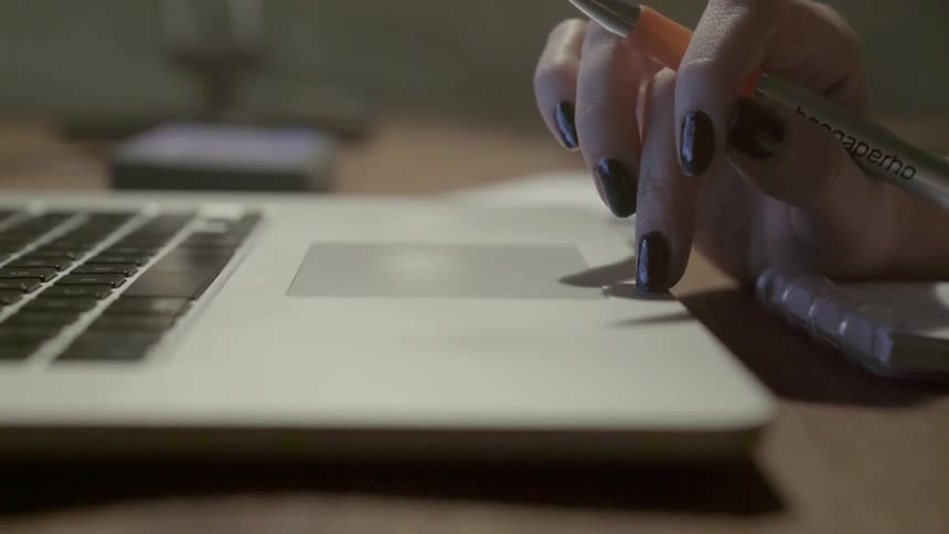 A person with dark nails uses a laptop trackpad while working at a desk.