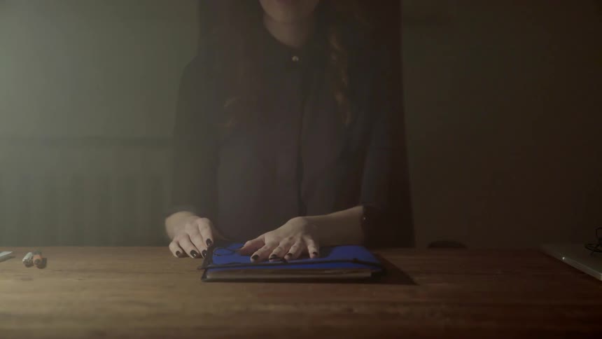 Moody shot of a person in black clothing closing a blue document portfolio shut.