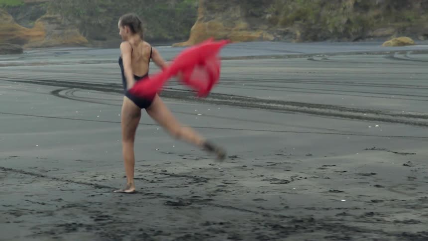 Woman wearing a swimsuit dances on a beach holding a red veil
