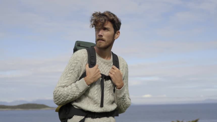 An ambitious backpacker explores a windy island hillside while looking for a campsite.