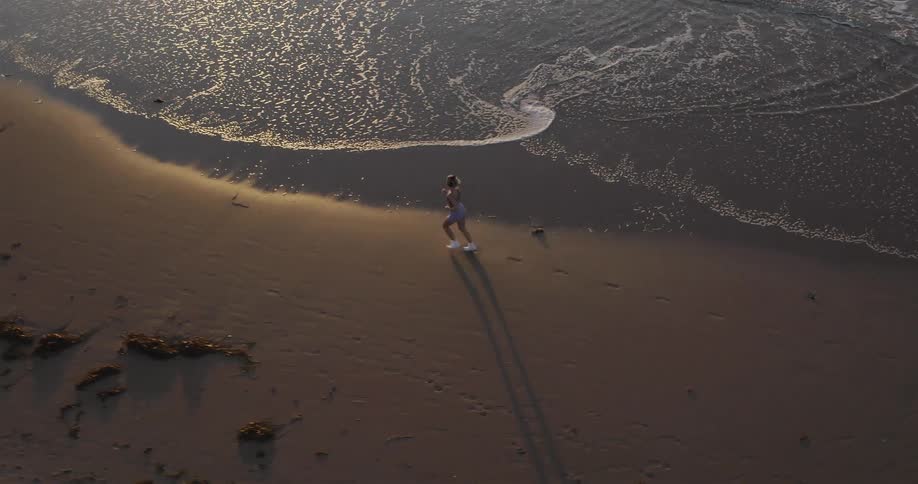 A woman jogs on the beach as waves roll into shore
