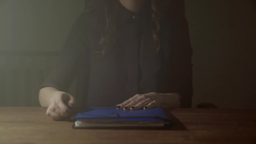 A woman sitting at a table closes a portfolio and secures it with a strap