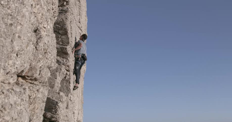 Male rock climber climbs up cliff side against a blue sky